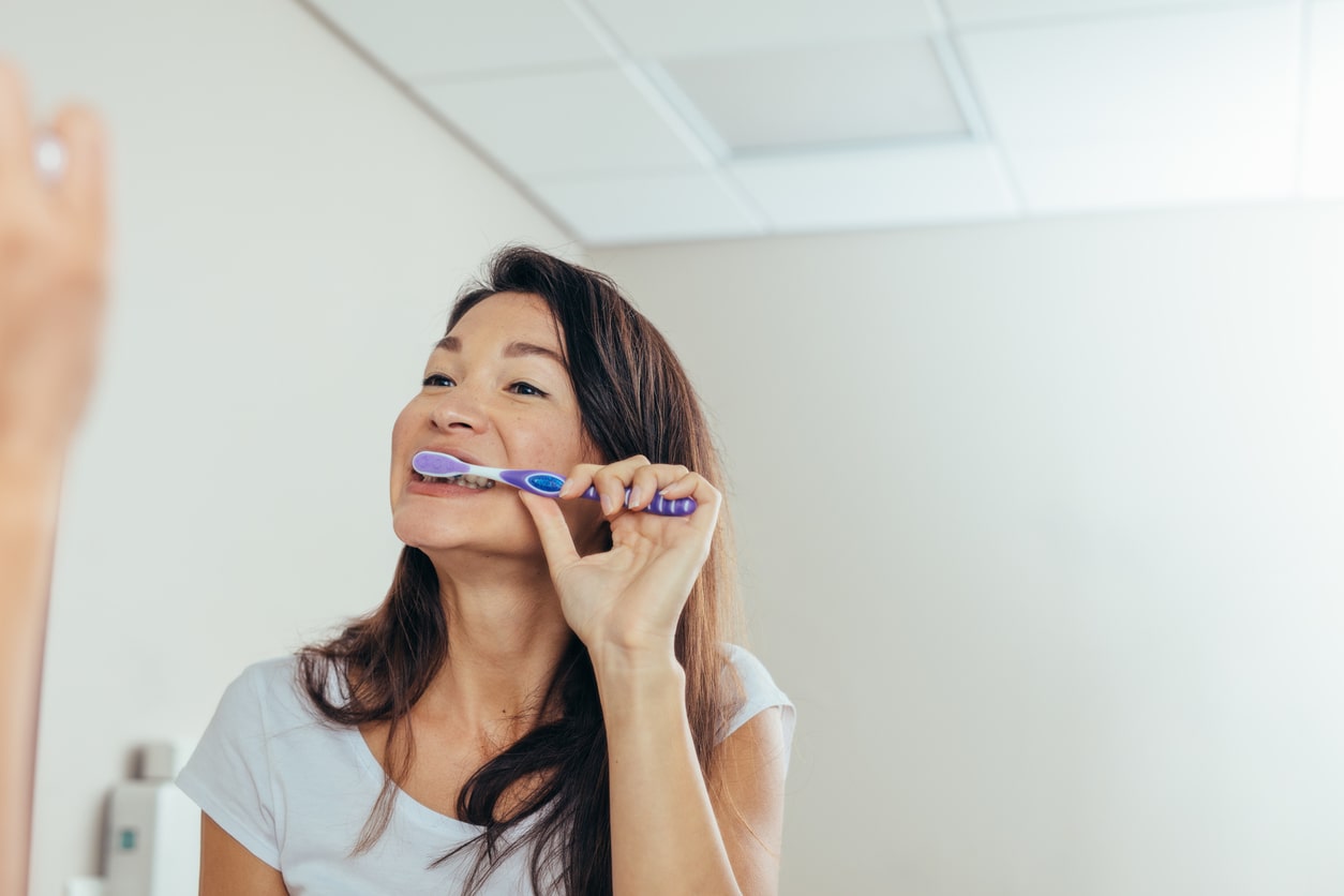 woman brushing teeth in mirror